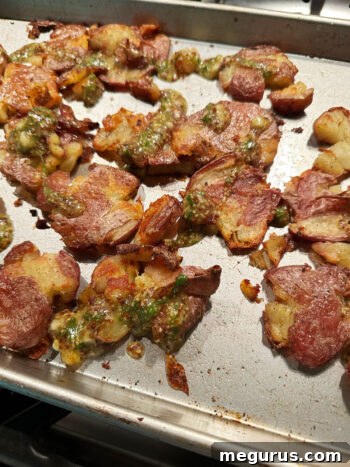Vinaigrette dressing being drizzled over hot, roasted smashed potatoes.