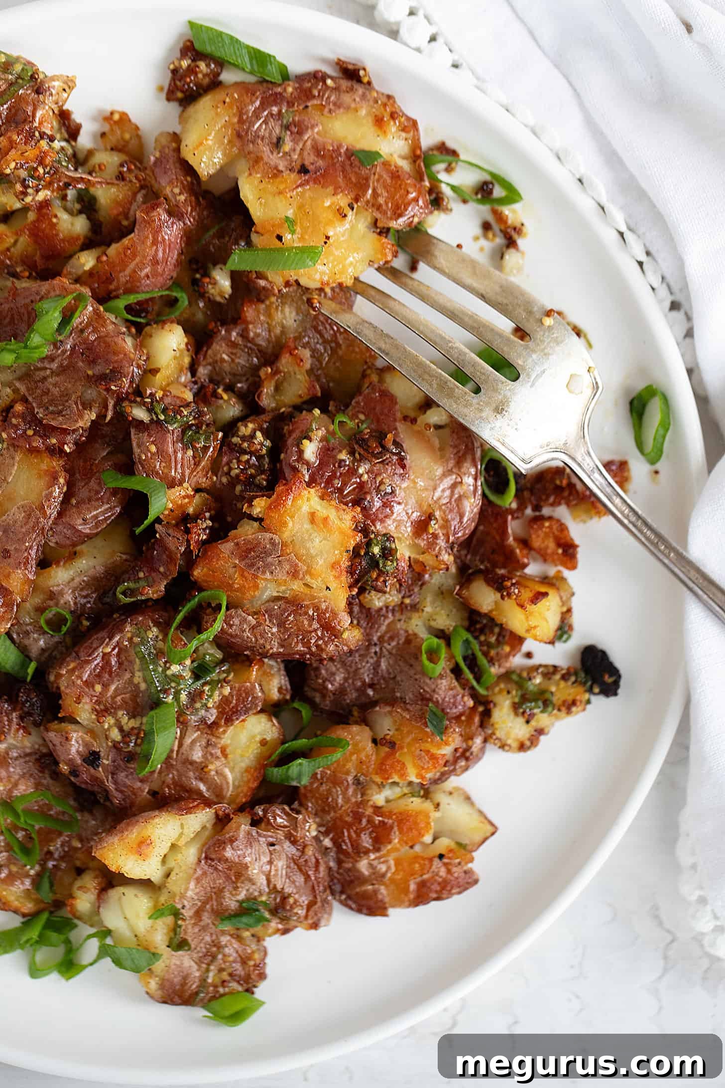A close-up of warm smashed potato salad on a white plate with a fork, highlighting the crispy texture.