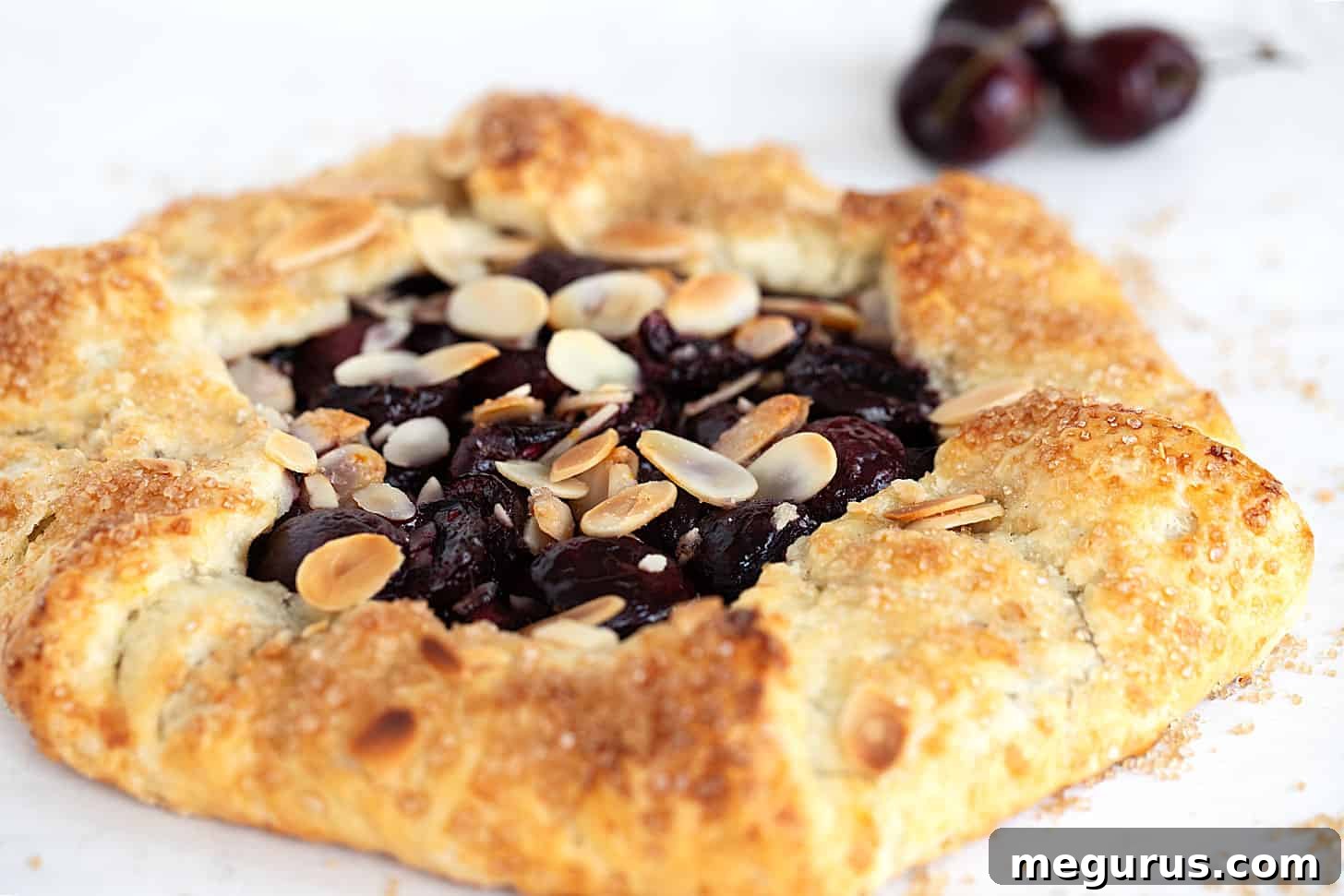 Delicious sweet cherry galette, topped with almonds and flaky crust, with fresh cherries in the background