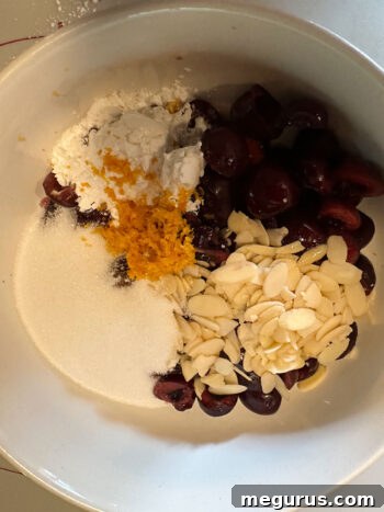Bowl containing all cherry filling ingredients: pitted cherries, sliced almonds, sugar, orange zest, orange juice, and cornstarch