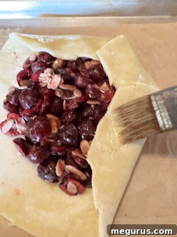 Partially folded galette pastry being brushed with egg wash, showing the rustic edge