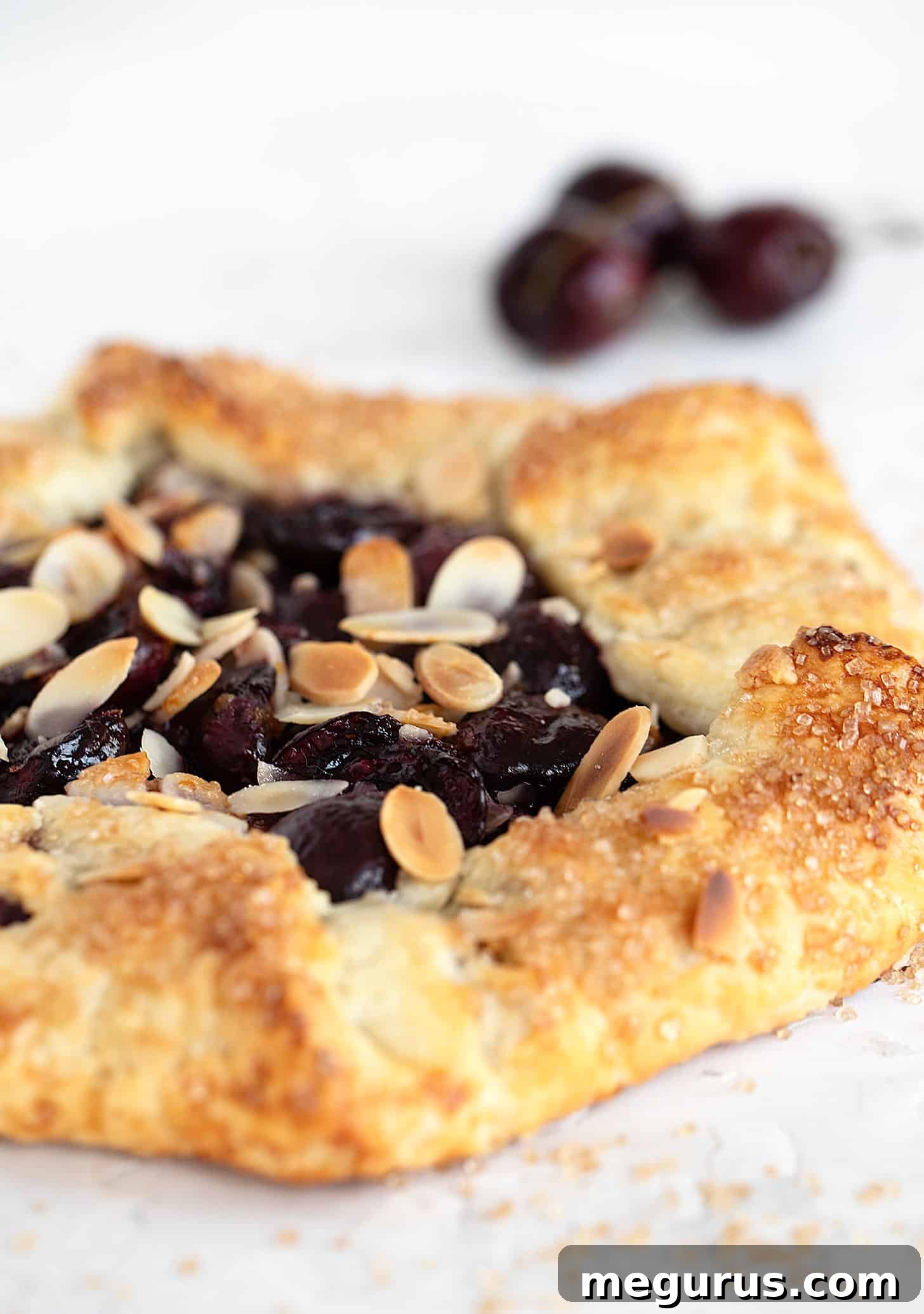 Freshly baked sweet cherry galette with a golden, flaky crust and bubbly filling, with more fresh cherries in the background