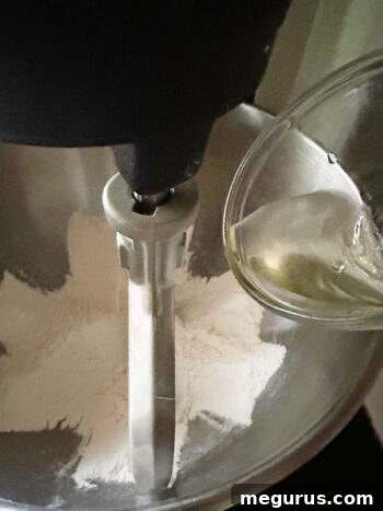 Adding vegetable oil to a mixture of flour, sugar, and salt in a stand mixer bowl