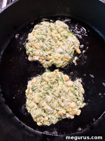 Fritters gently spread into thin rounds in the skillet, browning.