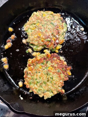 Golden-brown fritters in a skillet after being flipped to cook the second side.