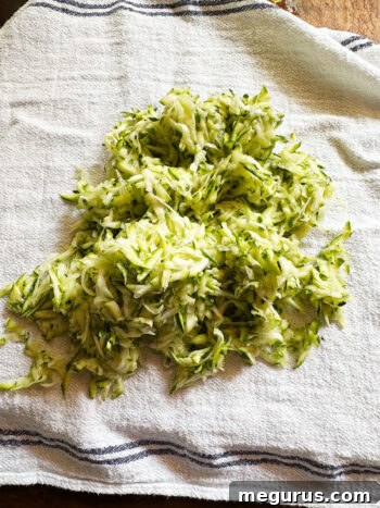 Grated zucchini resting on a clean tea towel, ready for moisture removal.