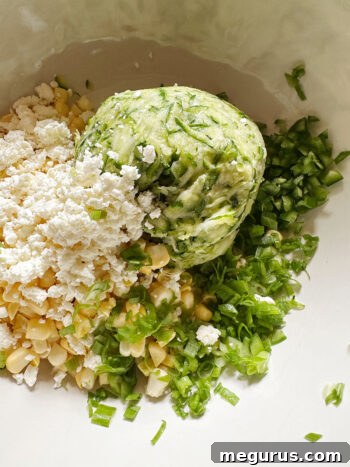 Bowl containing squeezed zucchini, corn, feta, diced jalapeño, and sliced green onion.
