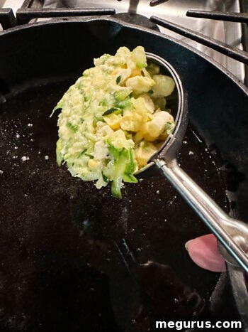 A scoop of fritter batter being placed into a hot skillet.