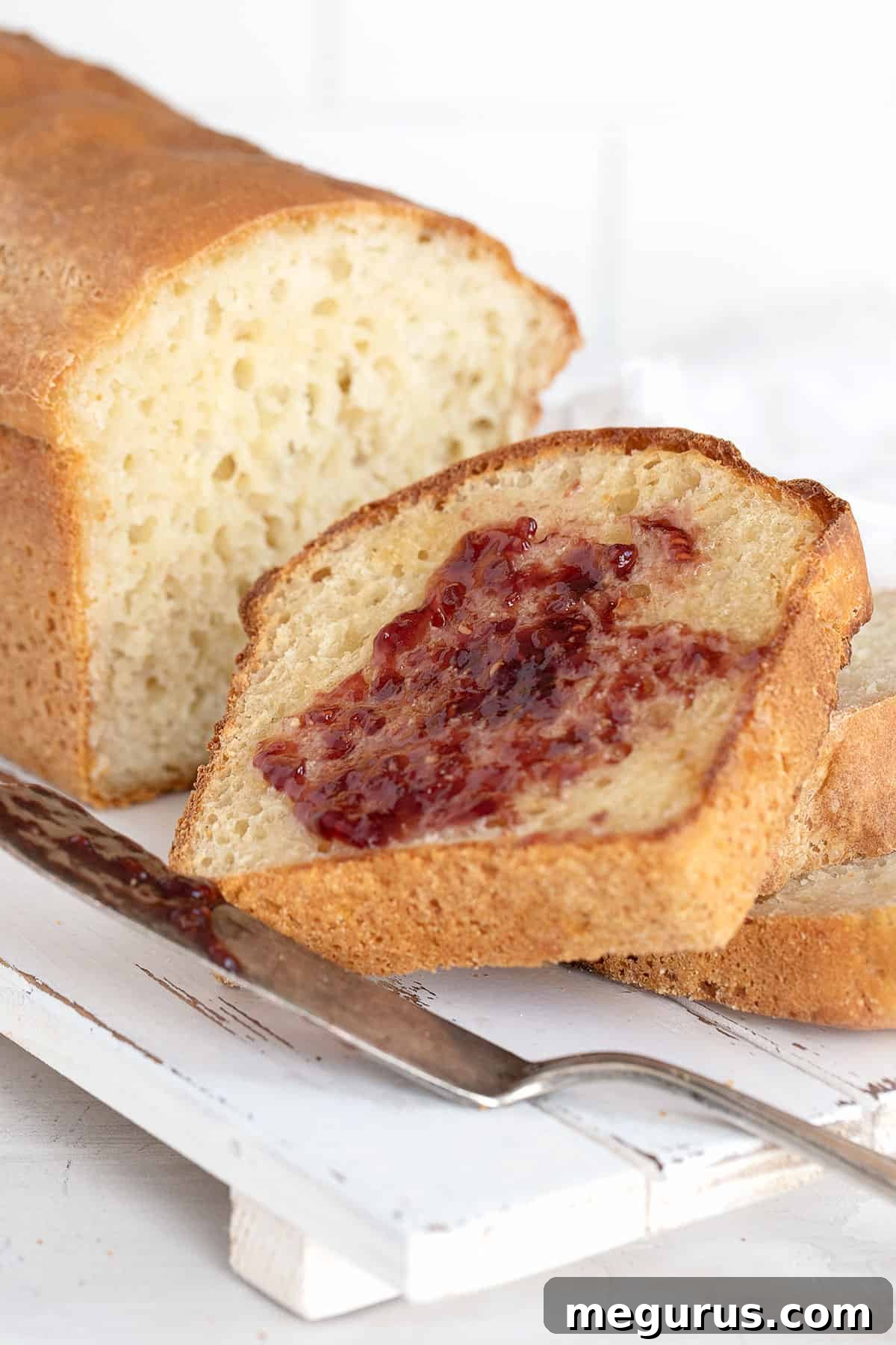 Close-up of English Muffin Bread, perfectly sliced with butter and jam, highlighting its signature porous texture.