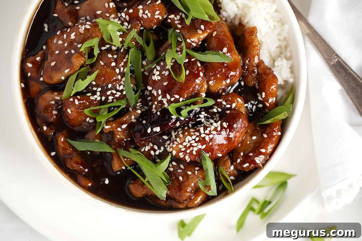 Mongolian pork in a bowl with white rice, garnished with fresh green onions and sesame seeds