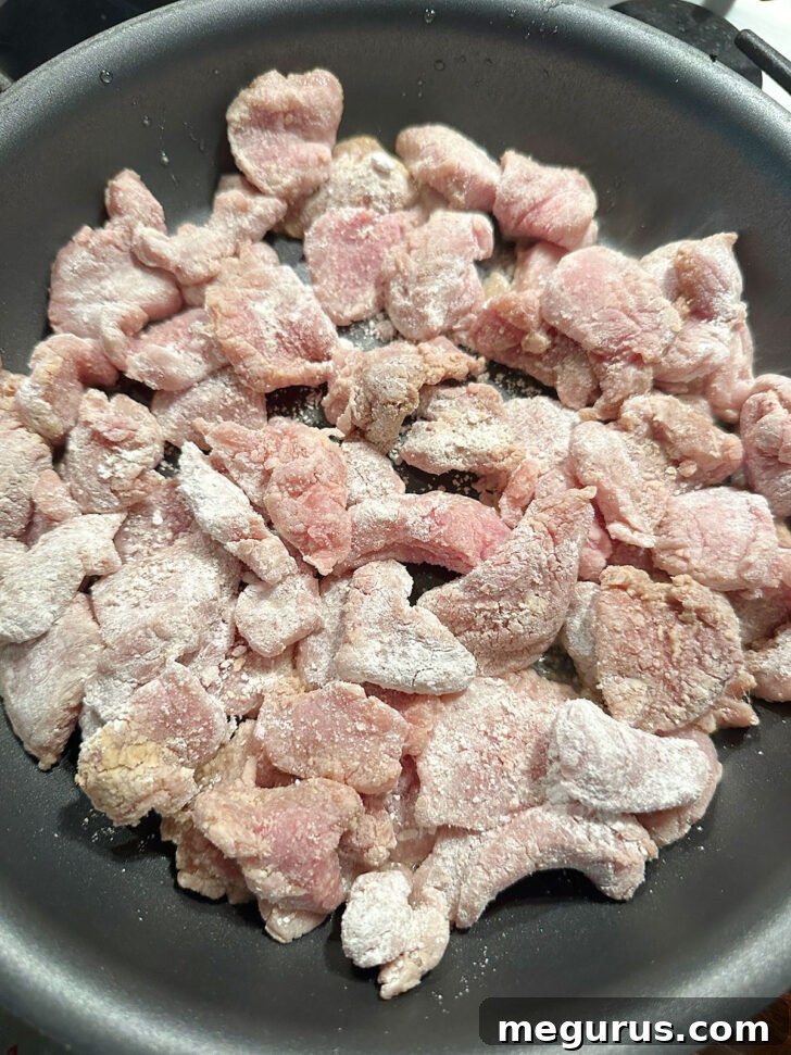 Adding cornstarch-coated pork strips to a hot skillet with oil