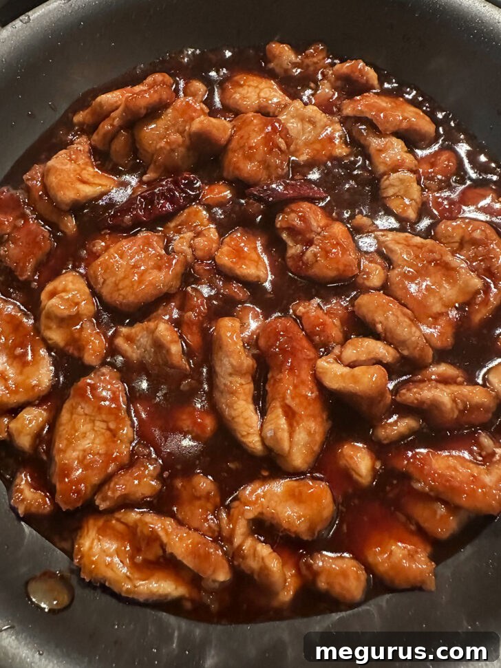 Finished Mongolian pork simmering in a skillet, coated in glossy sauce