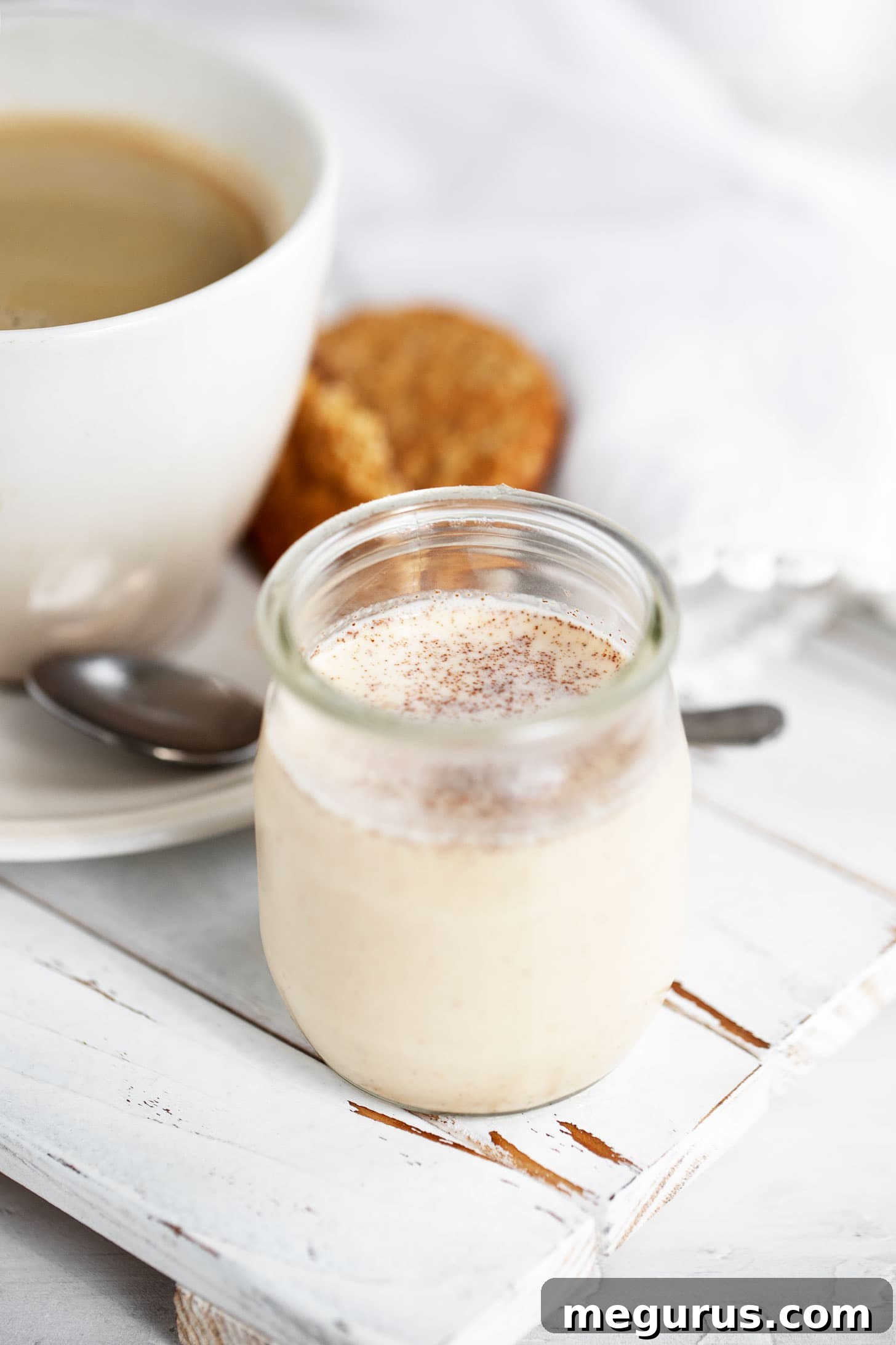 A glass bottle of homemade pumpkin spice coffee creamer next to a fresh cup of coffee, ready to be enjoyed.