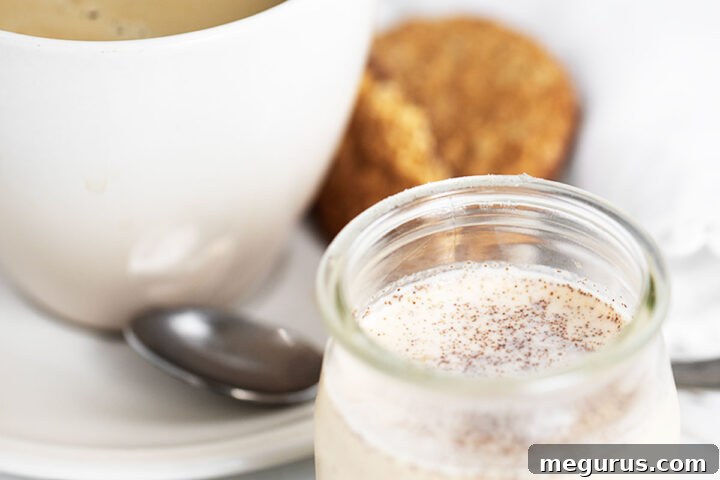 Close-up of a glass bottle of pumpkin spice coffee creamer, with a cup of coffee and fall decor in the background.