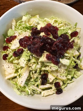 adding cranberries to bowl with Brussels sprouts and pear