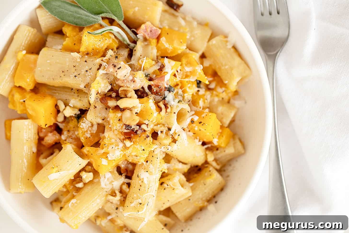 A beautifully plated bowl of roasted butternut squash pasta, garnished with fresh sage and a sprinkle of cheese.