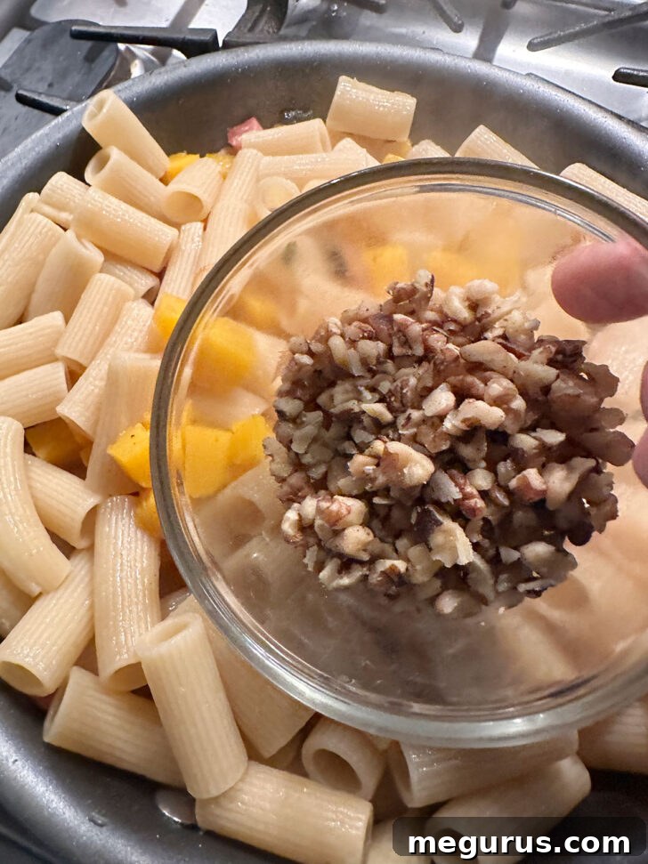 Chopped walnuts being sprinkled into the pasta and sauce mixture in the skillet.