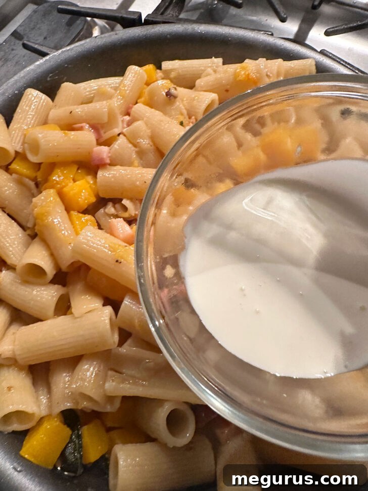 A drizzle of heavy cream being added to the finished pasta in the skillet.