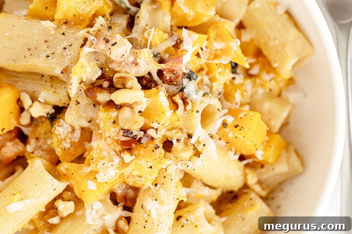 A bowl of roasted butternut squash pasta, garnished with fresh herbs and cheese.