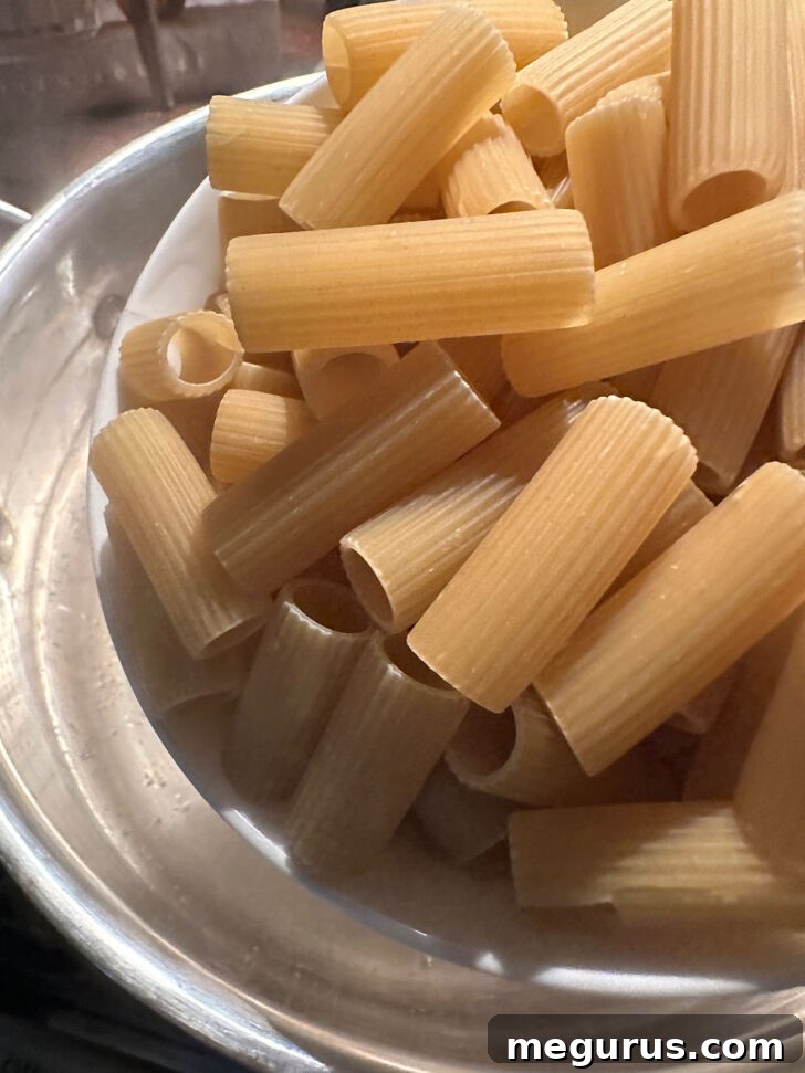 Rigatoni pasta being added to a large pot of boiling, salted water.