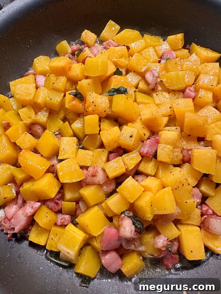 Roasted butternut squash being transferred into the skillet with the pancetta, shallots, and sage mixture.