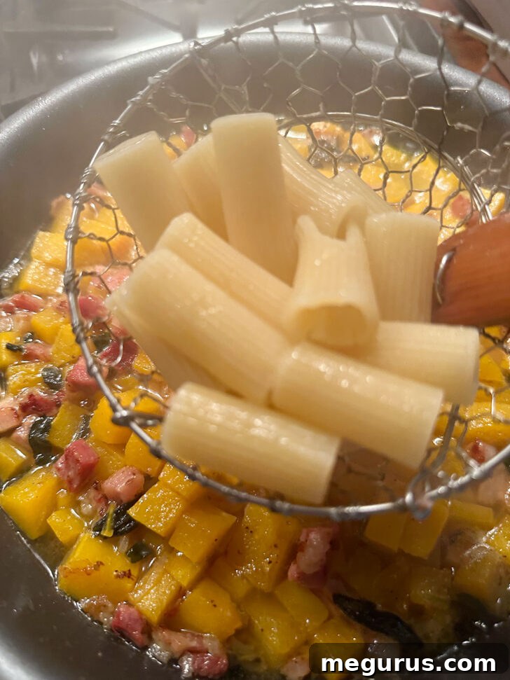 Cooked rigatoni pasta being added directly from the pot to the skillet with the sauce.