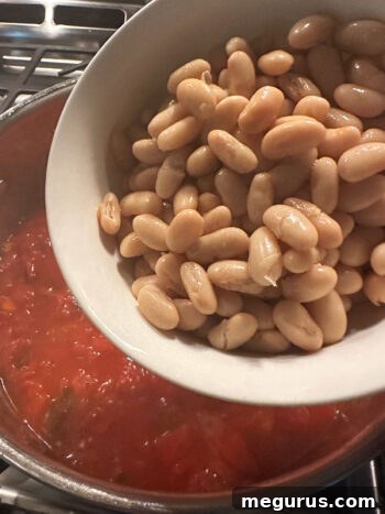 Adding drained cannellini beans to the pot.