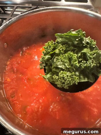 Fresh kale leaves being stirred into the simmering minestrone.