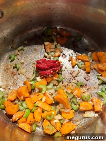 Adding tomato paste and red pepper flakes to sautéed vegetables in the pot.