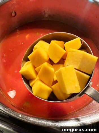 Diced butternut squash being added to the simmering soup base.