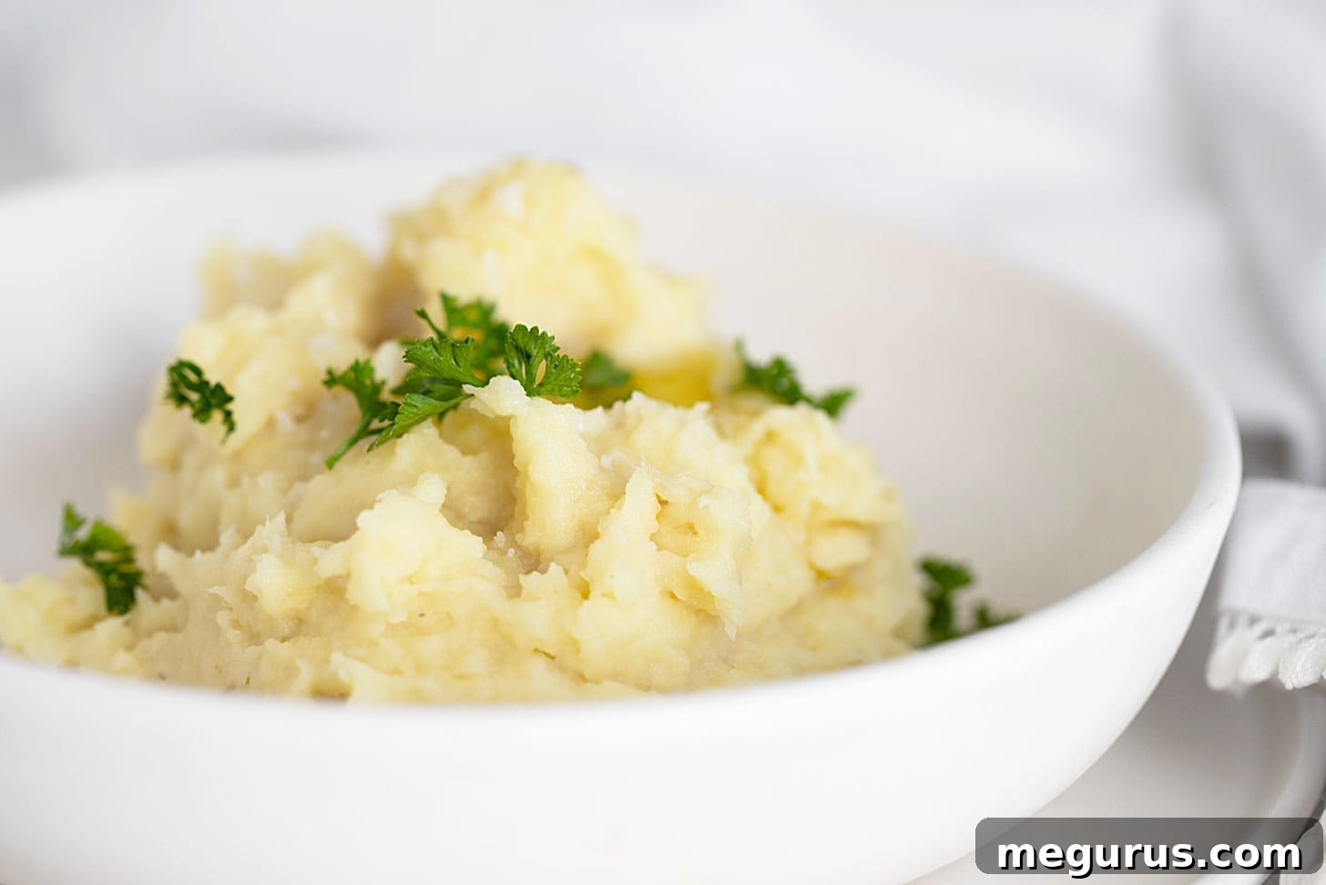 Parsnip puree in white bowl with parsley garnish, showcasing its creamy texture.