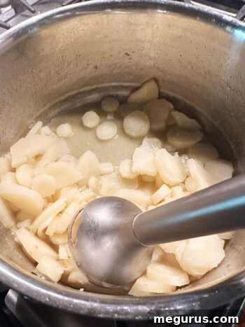 An immersion blender puréeing the cooked parsnips directly in the saucepan.