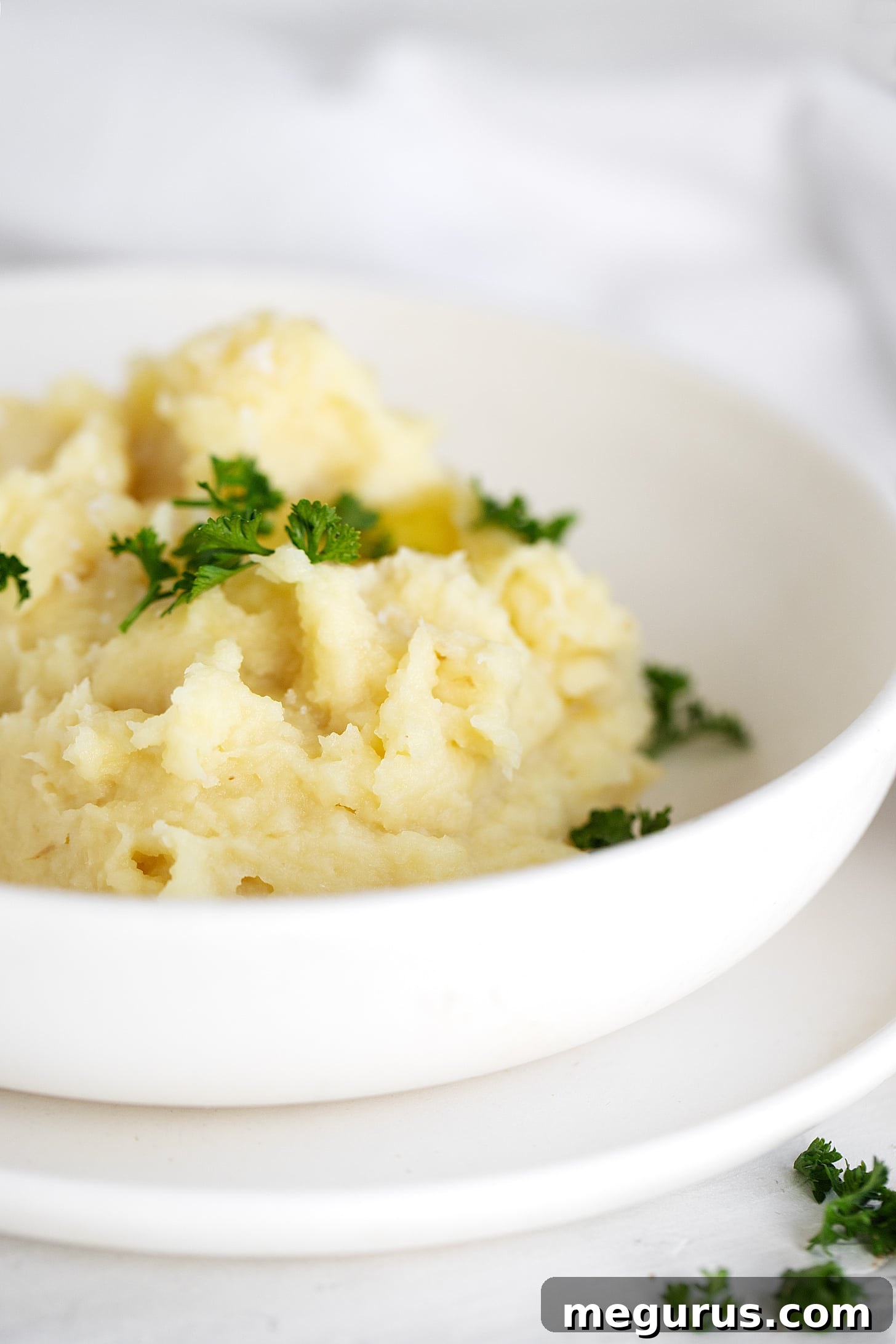 Buttery Parsnip puree in a white bowl, garnished with fresh parsley.