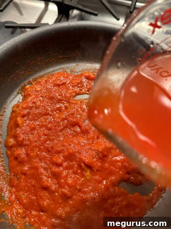 Pouring hot water into the skillet containing passata for the sauce base.