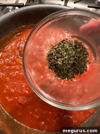 Adding dried fenugreek leaves to the simmering tikka masala sauce.