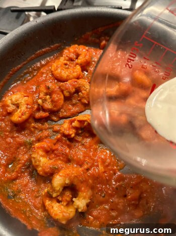 Pouring heavy cream into the skillet of shrimp tikka masala.