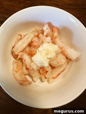 Adding ginger garlic paste to shrimp in a bowl for marination.