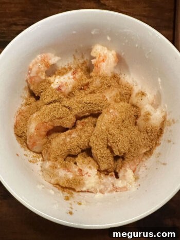 Adding a custom spice mix to the bowl of marinated shrimp.