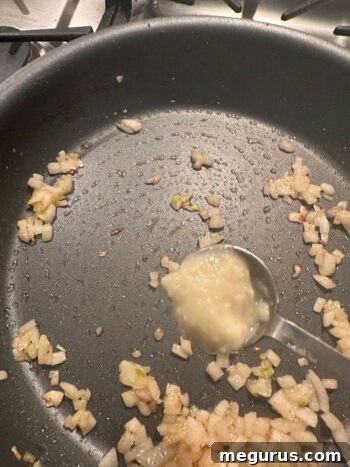 Adding ginger garlic paste to onions already cooked in a skillet.