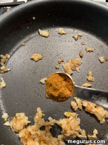 Adding the remaining spice mix to the skillet with onions and ginger garlic paste.