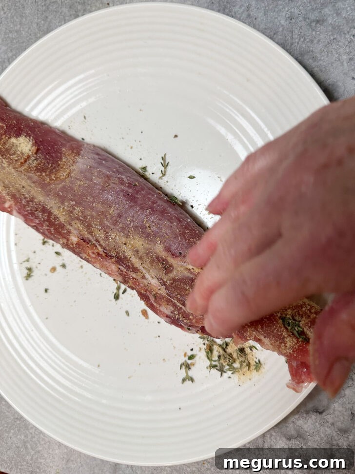 Rubbing spice rub evenly onto pork tenderloin before cooking.