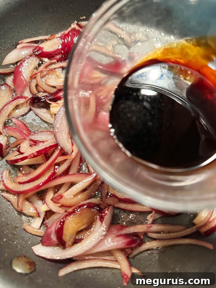 Adding balsamic vinegar to cooking onions in a skillet to create a rich glaze.