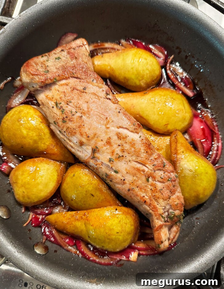 Pears, pork, and balsamic onions assembled in a skillet, prepared for oven roasting.