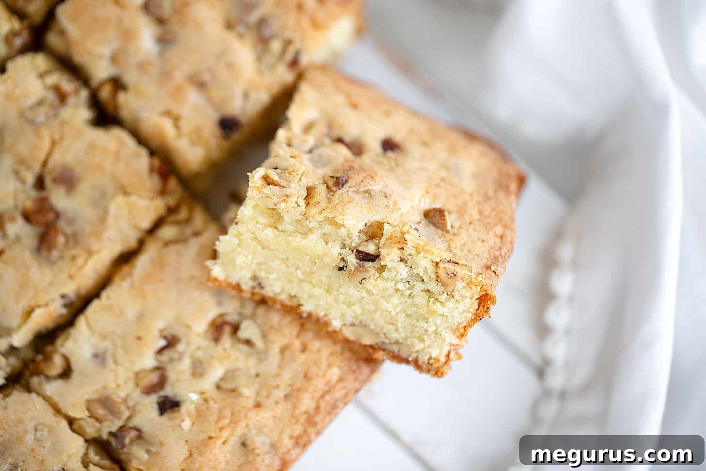 Maple walnut blondies sliced on a wooden board, showcasing their golden-brown crust and moist interior with visible walnuts.