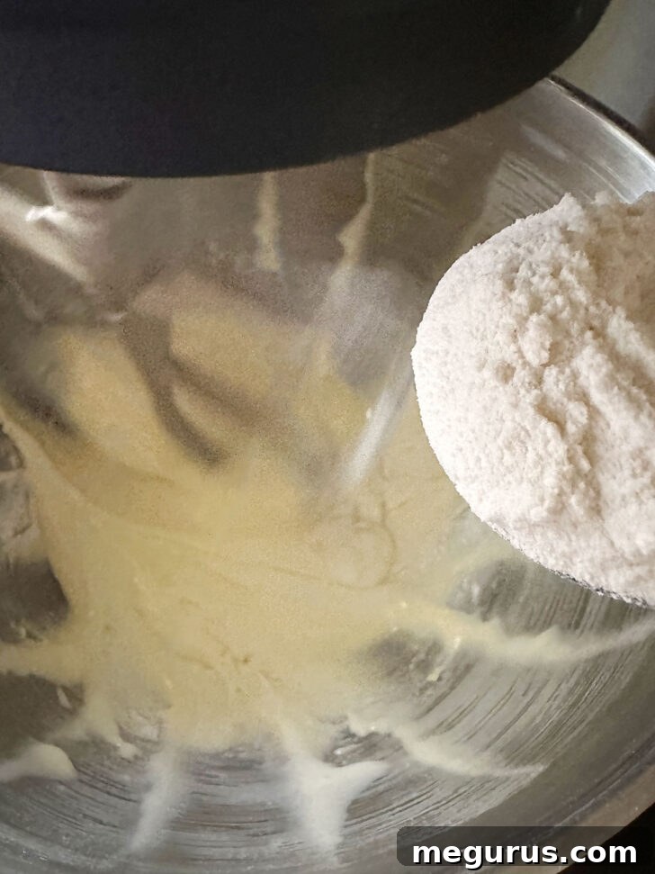 Dry flour mixture being added to the wet batter in a large mixing bowl.