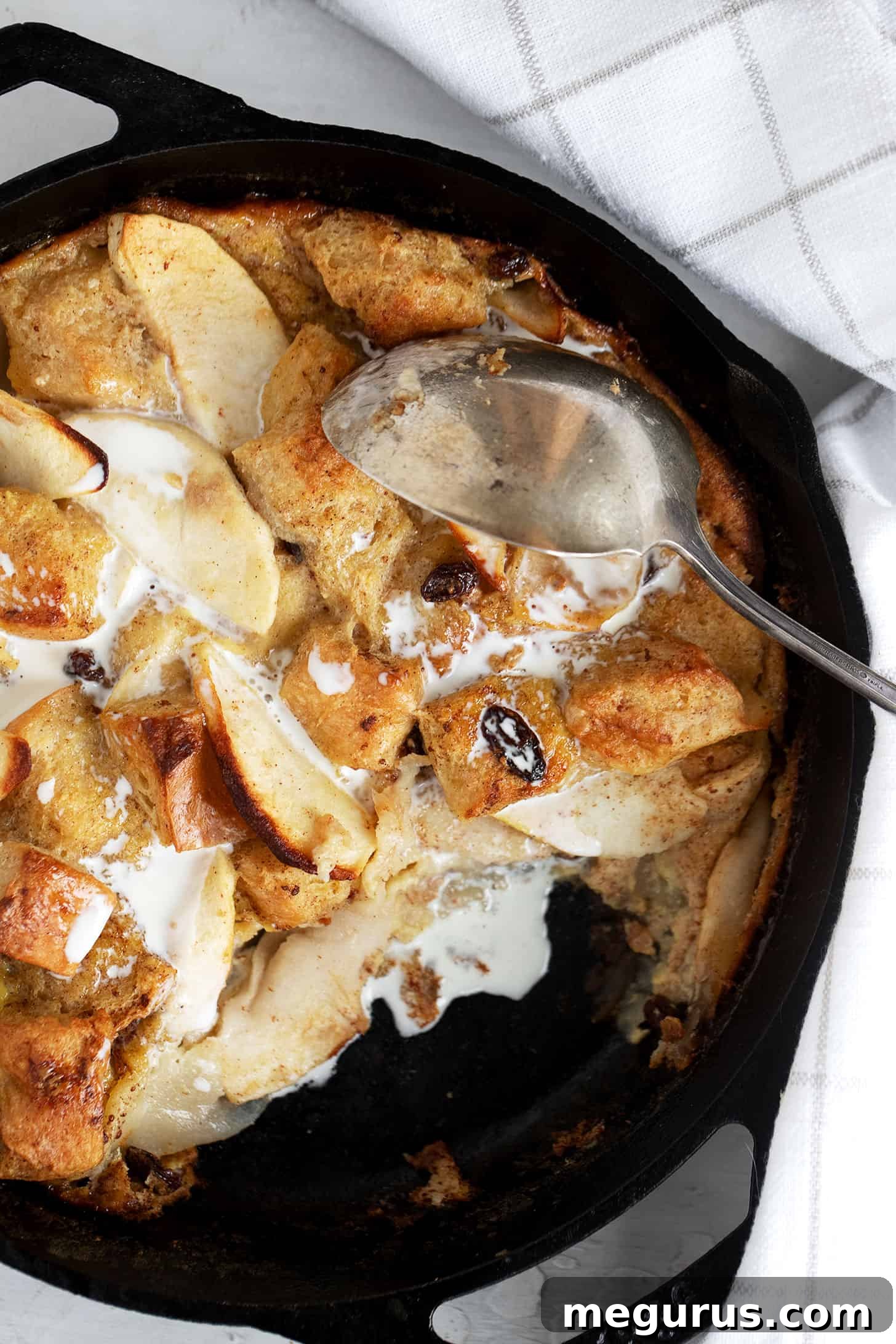 Close-up of baked apple bread pudding in a cast iron skillet, garnished with a light topping