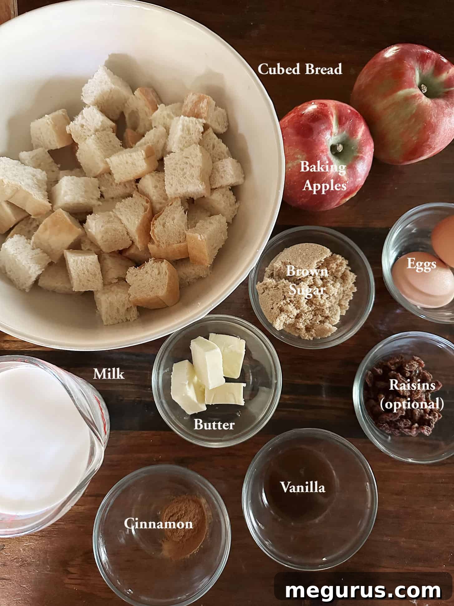 Fresh ingredients laid out for making apple bread pudding, including apples, bread, milk, eggs, butter, brown sugar, and vanilla