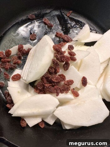 Adding prepared apples and raisins to the cast iron skillet for softening