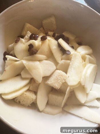 Transferring softened apples and raisins into a bowl with cubed bread