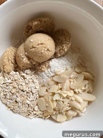 Dry crumble topping ingredients (brown sugar, flour, oats, almonds) in a bowl before butter is added.
